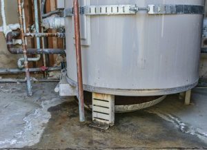 Water heater leaks from the bottom to the floor. Overflowing water heater drip pan. It is time to call a plumber service for inspection, repair or replacement