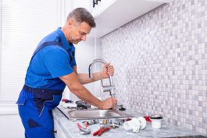 Side View Of A Plumber Fixing Water Tap In Kitchen